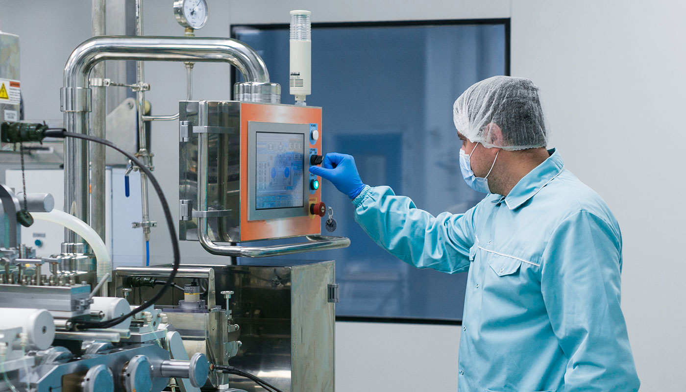 Mann mit blauen Overall und Haarnetz an einer Maschine in der Chemie-Industrie